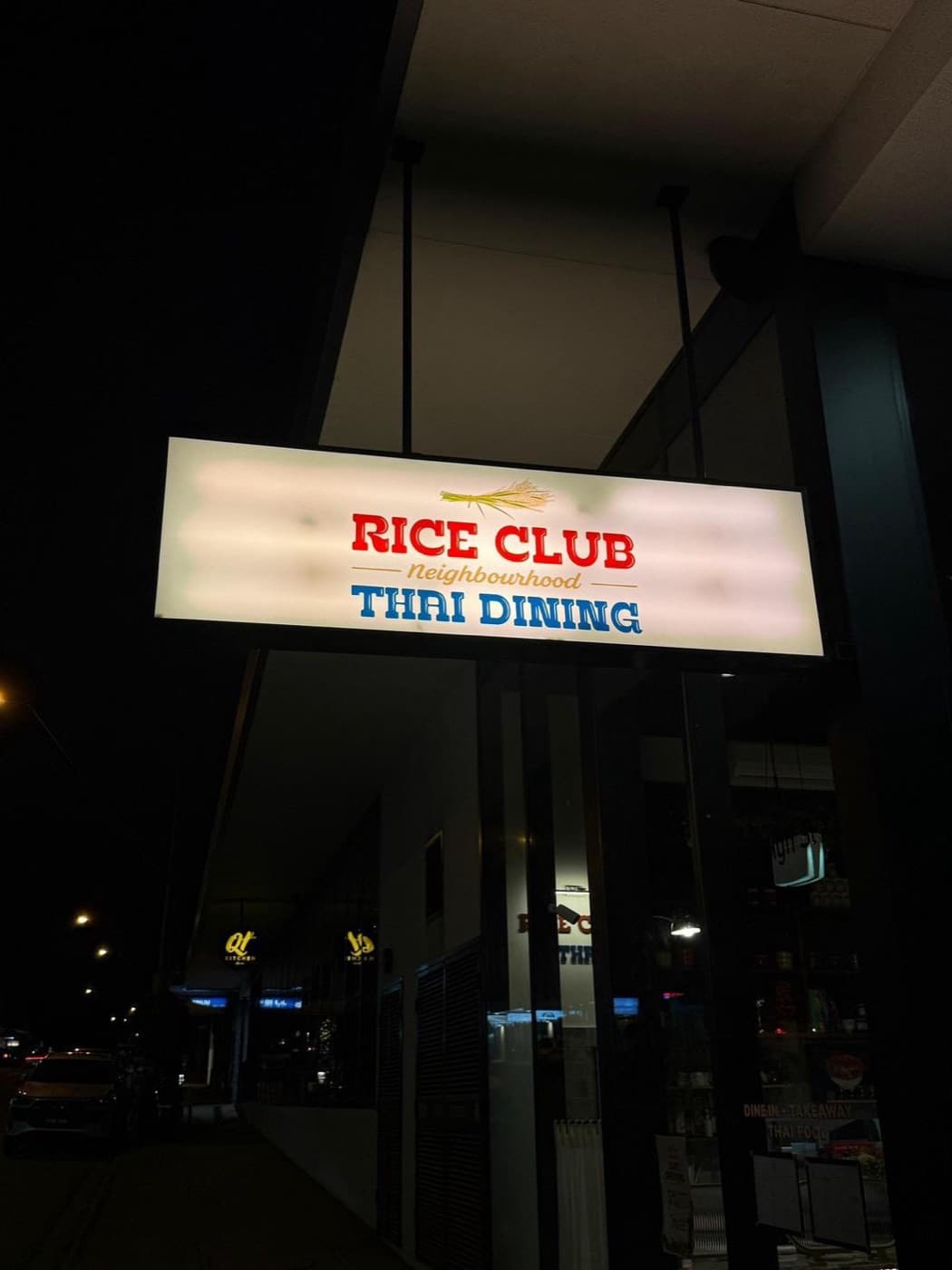 The lit 'Rice Club — Neighbourhood Thai Dining' sign above the High Street shopfront at night